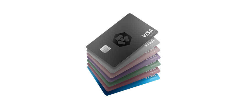 Stack of Crypto.com Visa Signature credit cards in various colors, including a black metal card on top with the Crypto.com lion logo. The cards are arranged in a sleek fan pattern against a dark background, emphasizing the premium metallic design.