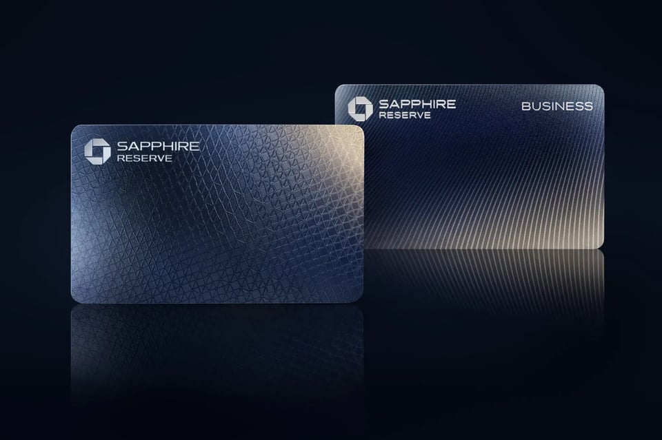 Two dark blue metallic credit cards labeled “Sapphire Reserve” and “Sapphire Reserve Business” with sleek, minimalist designs on a black background.