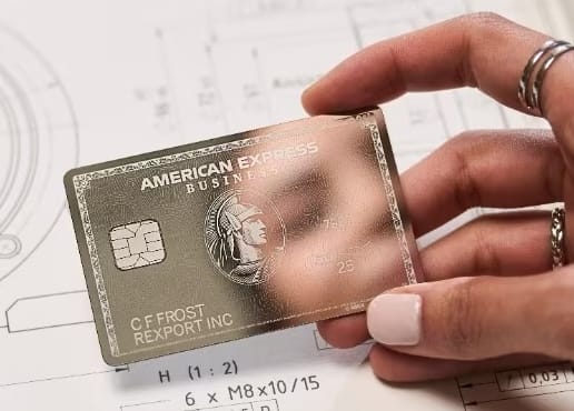 Hand with rings on fingers holding an American Express card. The card reflects a face in the mirror-finish.