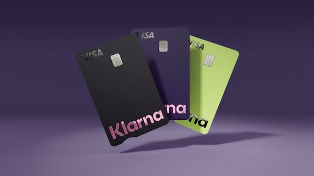Three vertical-oriented credit cards, fanned out. The black card on top shows the Visa logo and the Klarna logo. The middle card is dark blue. The bottom card is yellow-green.