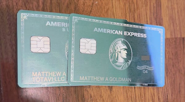 Two mirror-finish American Express Platinum cards stacked on top of one another on a wood background.