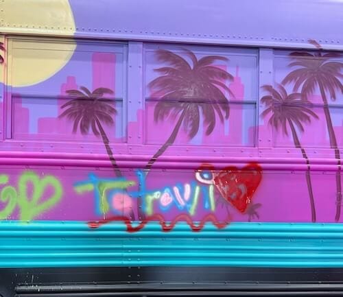 A colorfully painted school bus with palm trees, the spray-painted word "Totavi" and a heart.