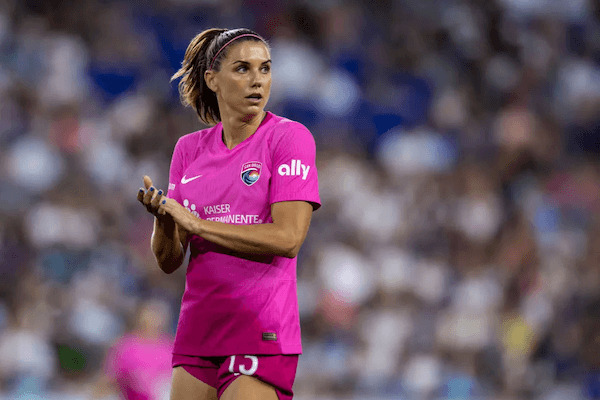 Soccer player with brown hair wearing a bright pink uniform with the San Diego Wave logo and the Ally bank logo on the sleeve.
