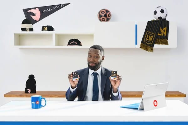 The BMO spokesman sitting at his desk, holding branded cards and surrounded by Angel City FC and Los Angeles FS merchandise.