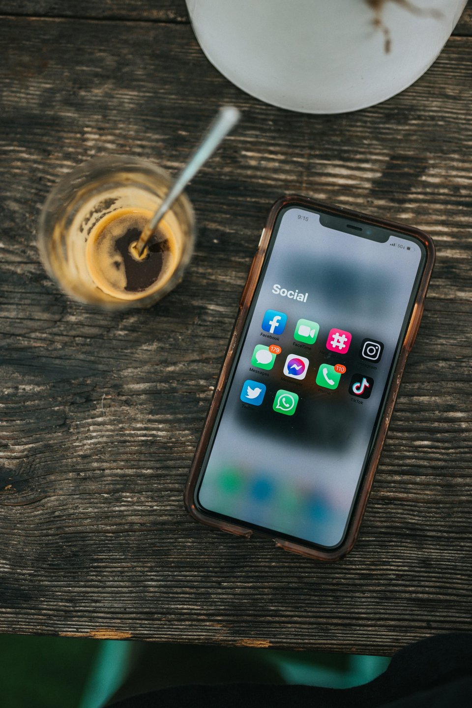 Image of a smart phone on a table next to a coffee. The screen shows social media app icons. Photo by Nathan Dumlao on Unsplash.