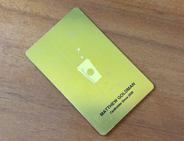 A gold credit card with a Starbucks cup and a two stars on a wood background.