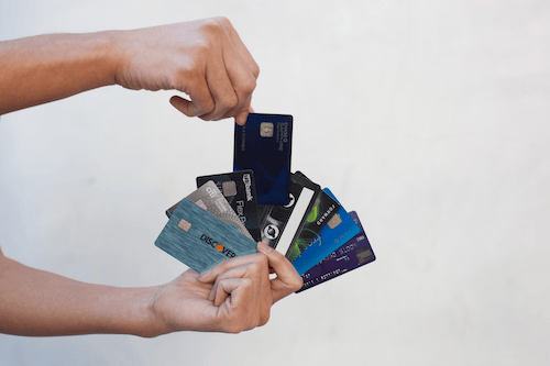 Human hand holding a group of credit cards, fanned out to show each card. Another hand reaches from the top to pull out the Chase Sapphire Reserve card. Background is neutral.